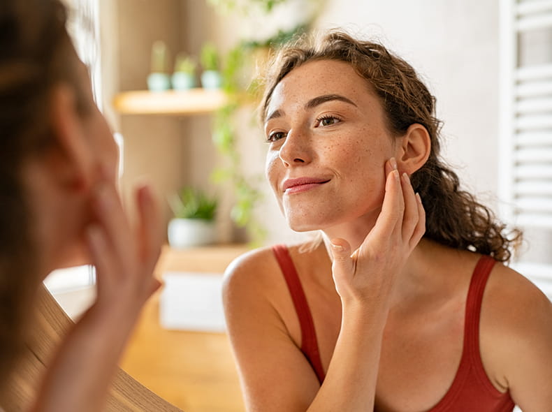 Dermatology image of photo applying cream to her face looking in the mirror.