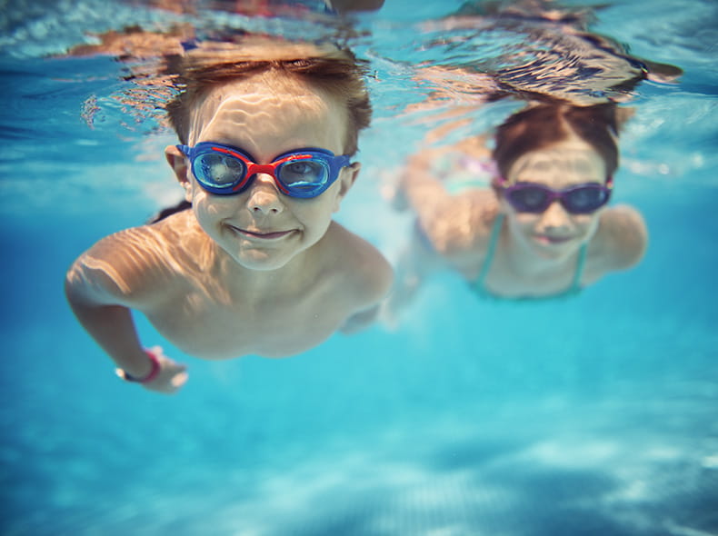 two children swimming in a pool with swim goggles on