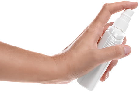 A hand holding a small white spray bottle, with the index finger pressing down on the nozzle.