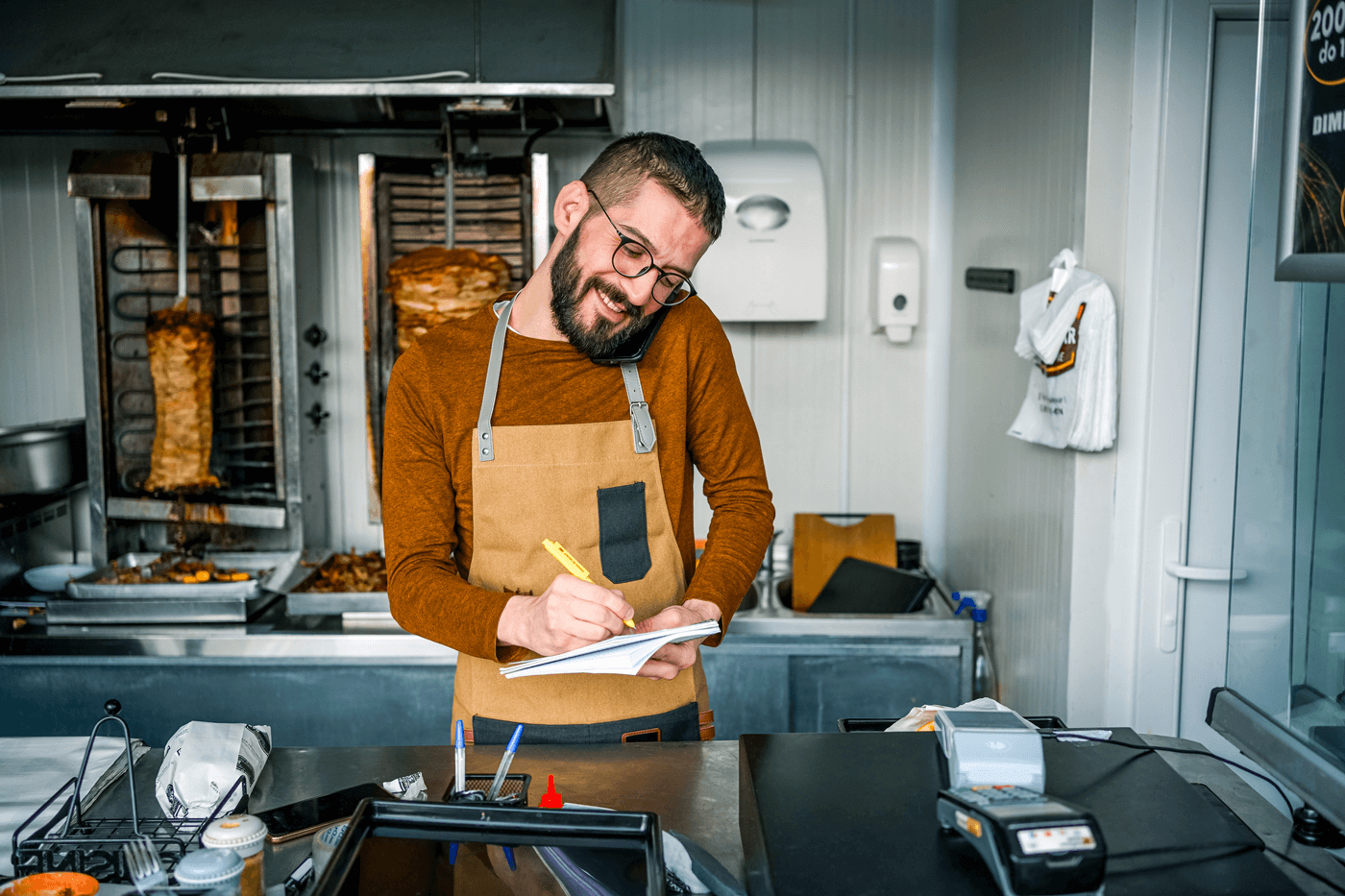 A chef at a kebab shop takes notes while on a phone call
