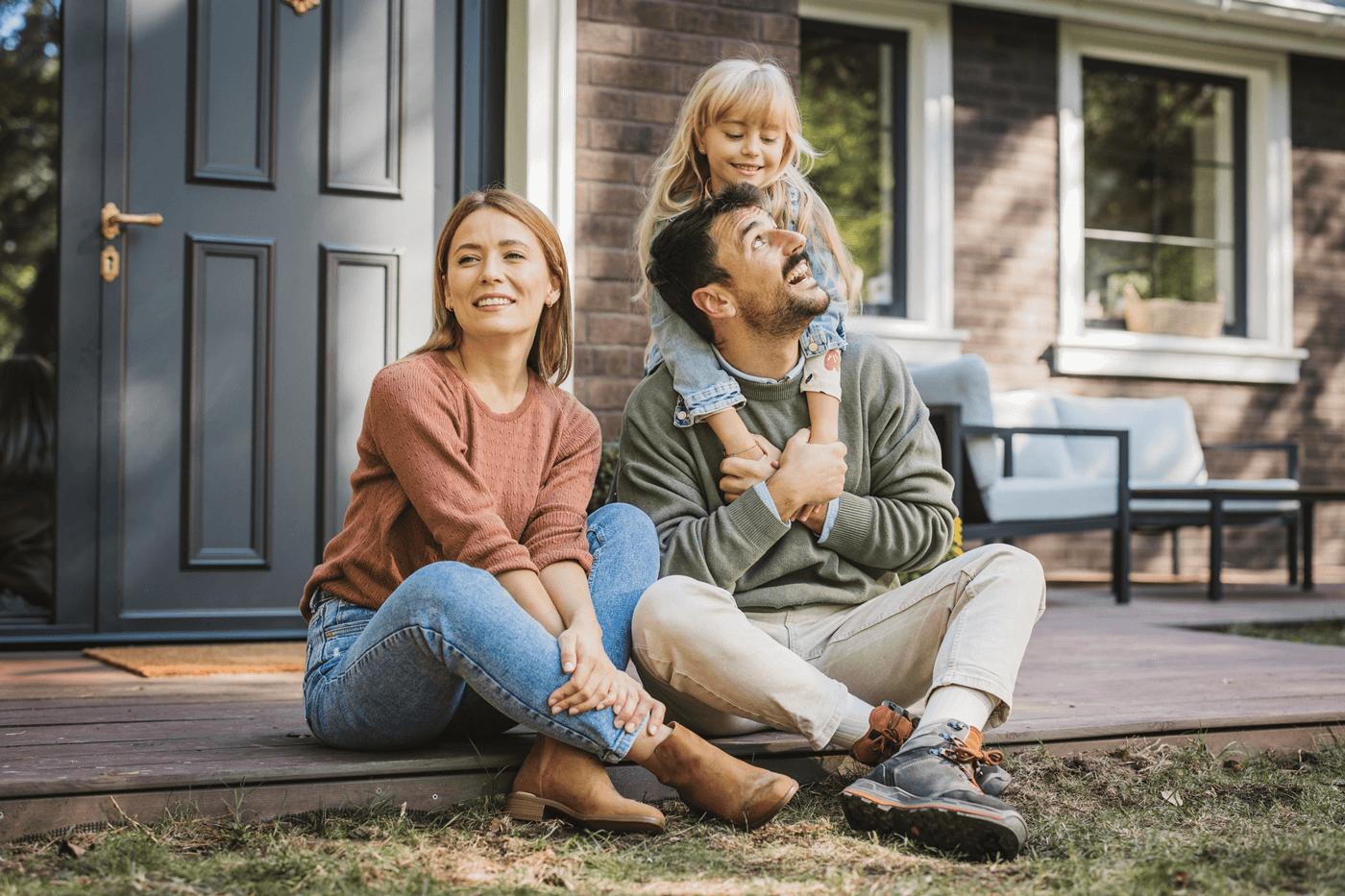 A young family sits outside their home