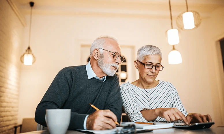 An elderly couple do calculations at a desk with pencil and paper