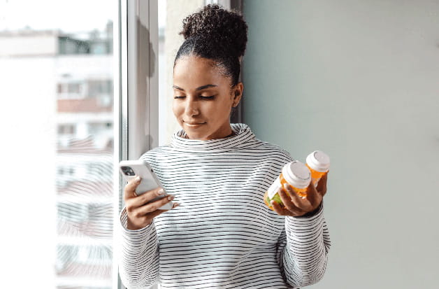 A woman holds prescription bottles while consulting her phone