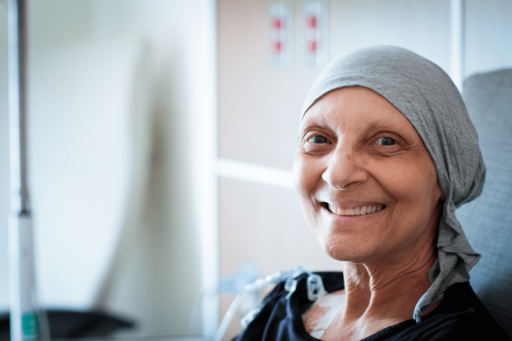 A senior patient in a hospital wearing a headwrap smiles into the camera