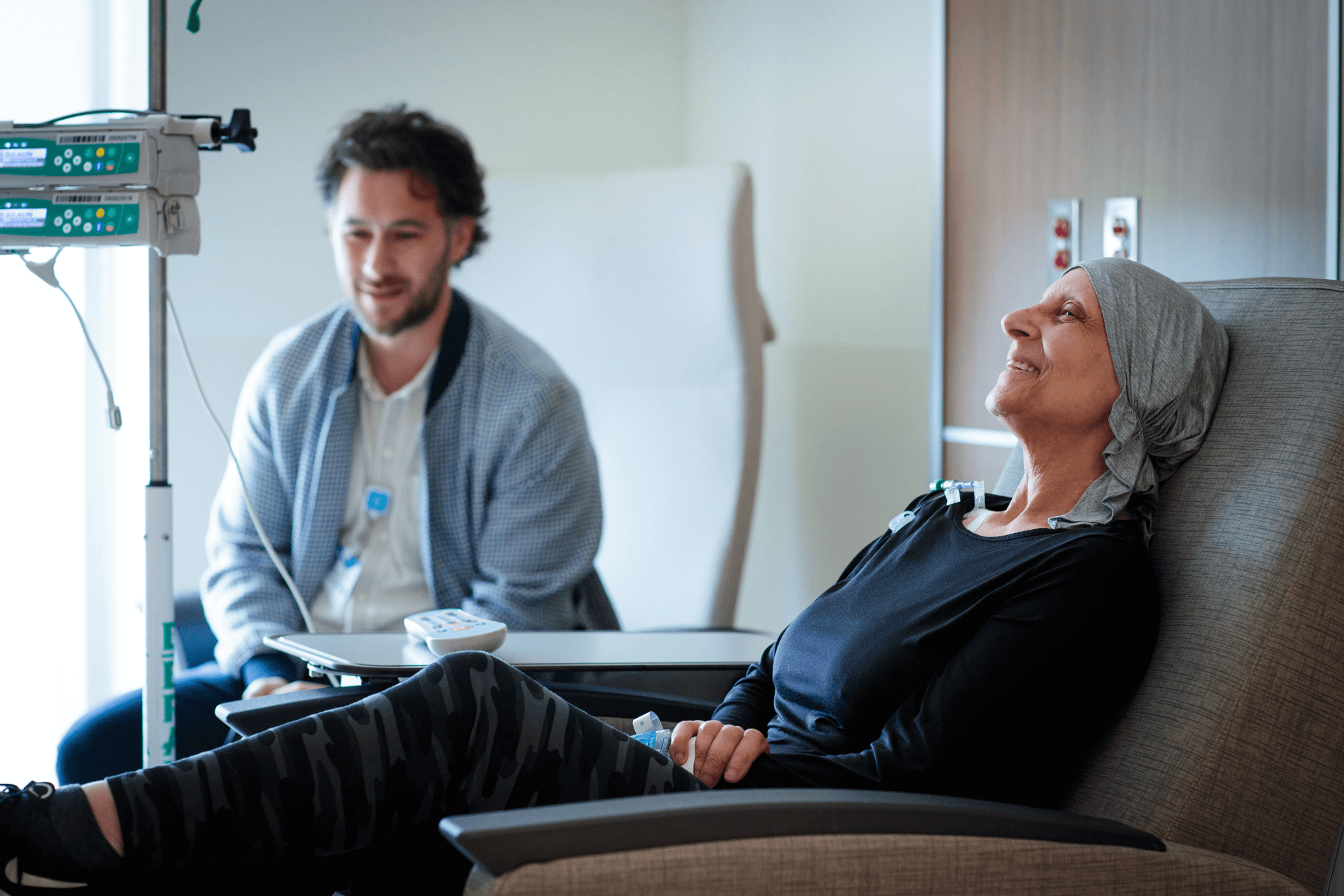 A senior patient sits in a chair in a hospital with a family member seated nearby