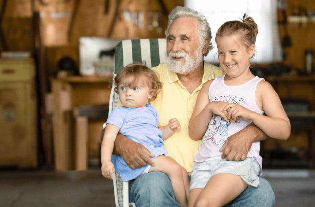 A senior holds two grandchildren on his lap