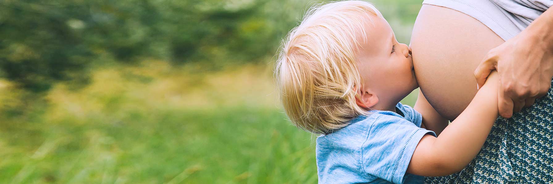 expecting mother and son after sport practice standing behind a car