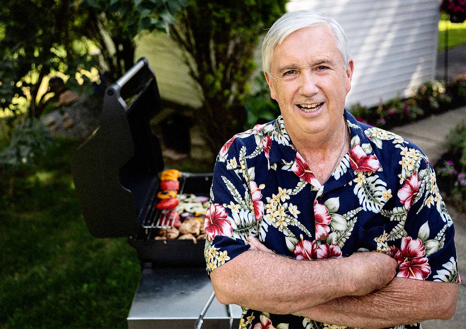 An older man in a Hawaiin shirt relaxes in his backyard.